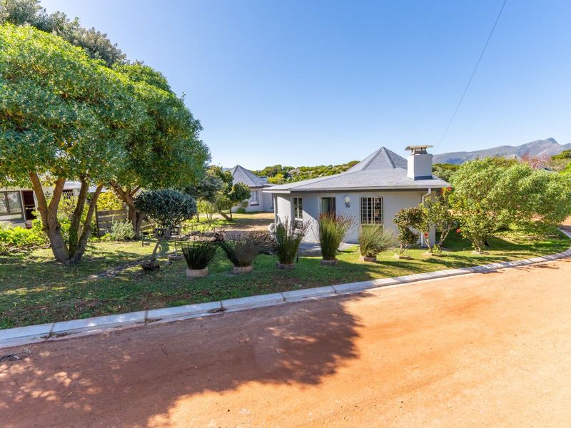 A charming single-story cottage with a tiled roof and chimney, set within a well-maintained garden in a quiet residential area.