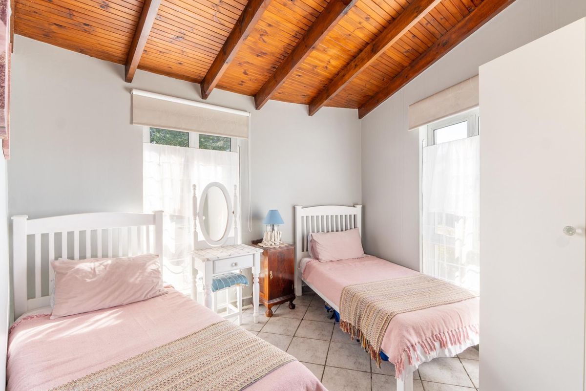 A bright bedroom featuring a vaulted timber beam ceiling, tiled flooring, and built-in storage, offering a cozy and well-maintained living space.