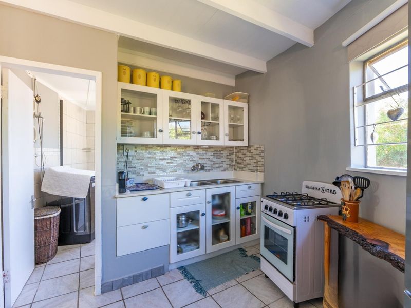 A functional kitchen featuring built-in cabinetry, a gas stove with oven, mosaic tile backsplash, and tiled flooring, with an adjacent laundry area visible.
