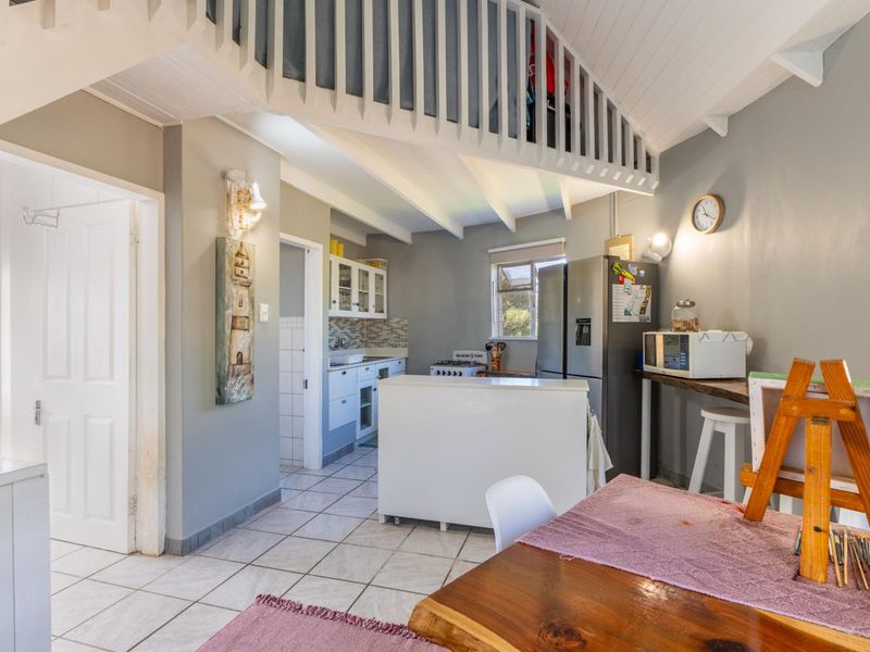 Open-plan living area featuring tiled floors, exposed beam ceilings, a mezzanine level, and a functional kitchen with built-in cabinetry and a tiled backsplash.