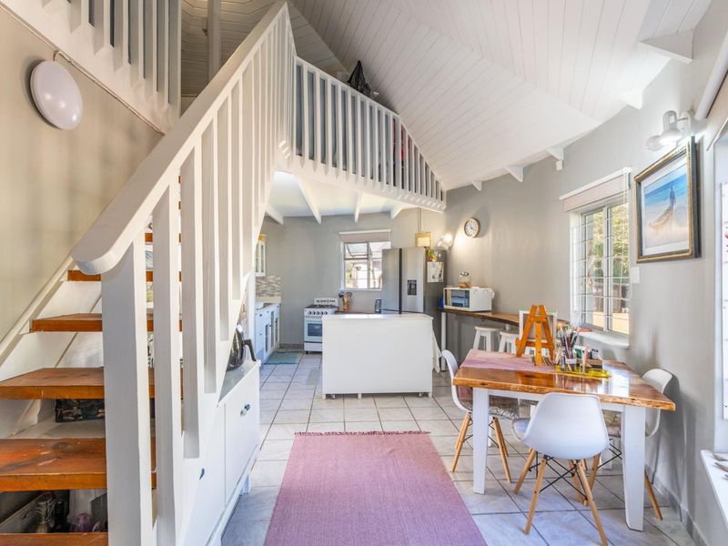 Open-plan living and kitchen area featuring a mezzanine level, staircase with timber treads, tiled flooring, and functional kitchen cabinetry.