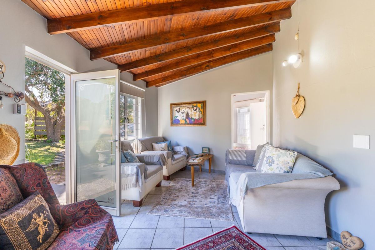 A bright living room featuring an exposed timber beam ceiling, tiled flooring, and direct access to the garden through a glass panel door.