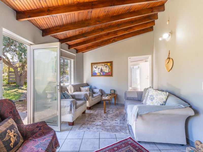 A bright living room featuring an exposed timber beam ceiling, tiled flooring, and direct access to the garden through a glass panel door.