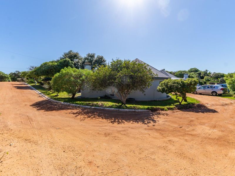 A view of the property exterior featuring a tiled roof and chimney, situated on a dirt road with surrounding landscaped garden area.