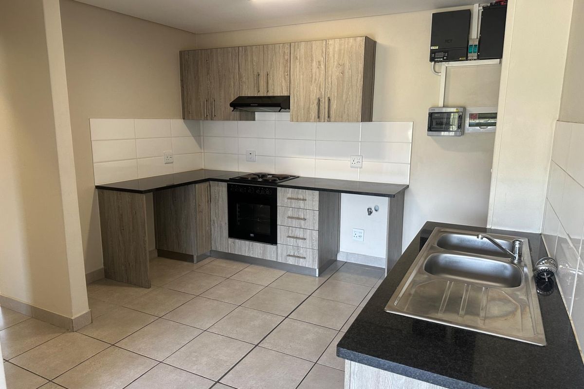 Modern kitchen featuring light wood-grain cabinetry, dark countertops, built-in oven and hob, and a double stainless steel sink with tiled flooring.