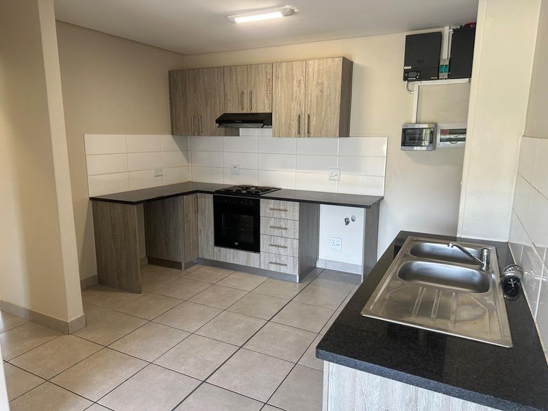 Modern kitchen featuring light wood-grain cabinetry, dark countertops, built-in oven and hob, and a double stainless steel sink with tiled flooring.