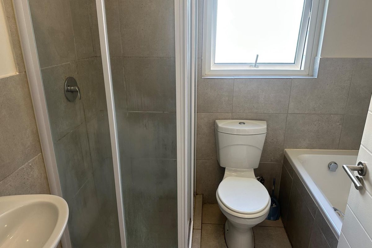 A functional bathroom featuring a shower enclosure, bathtub, toilet, and basin with neutral wall and floor tiling.
