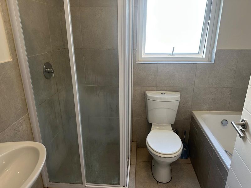 A functional bathroom featuring a shower enclosure, bathtub, toilet, and basin with neutral wall and floor tiling.