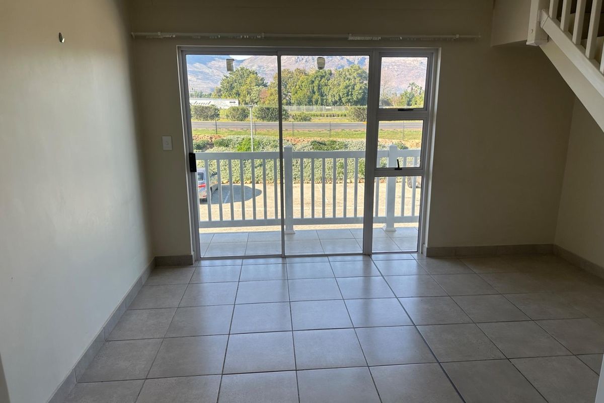 An empty living area featuring neutral tiled flooring, a staircase, and large sliding glass doors leading to an outdoor balcony with scenic views.
