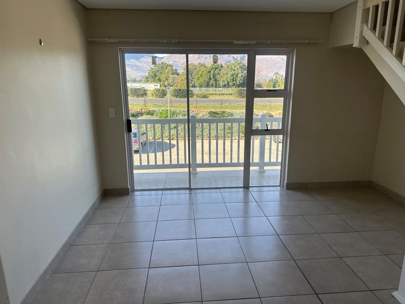 An empty living area featuring neutral tiled flooring, a staircase, and large sliding glass doors leading to an outdoor balcony with scenic views.