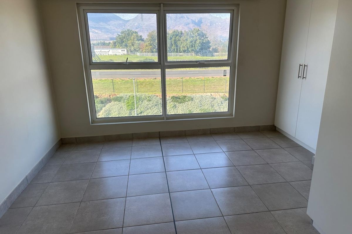 A bright, empty bedroom featuring neutral tiled flooring, built-in cupboards, and a large window offering scenic mountain and landscape views.