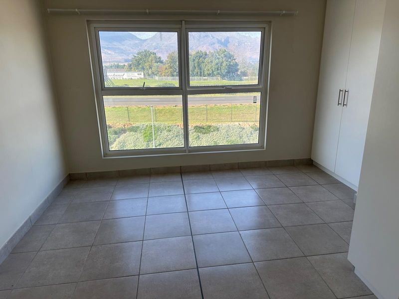 A bright, empty bedroom featuring neutral tiled flooring, built-in cupboards, and a large window offering scenic mountain and landscape views.