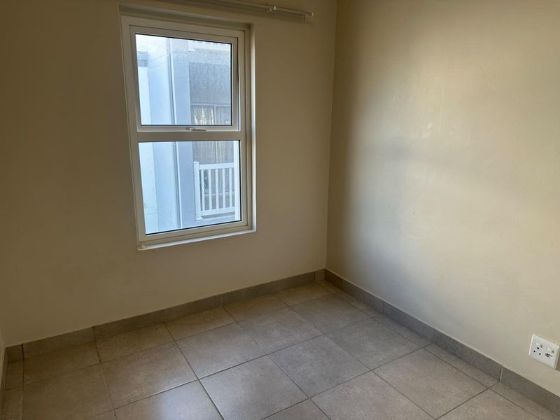 A vacant bedroom featuring neutral tiled flooring, plain walls, and a single window, providing a blank canvas for interior design.