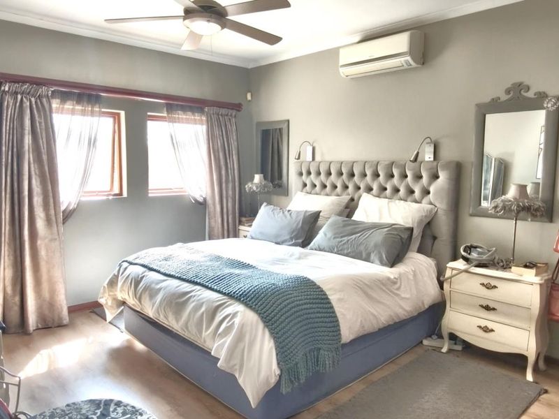 A well-maintained bedroom featuring laminate flooring, a ceiling fan, and a wall-mounted split-system air conditioner for climate control.