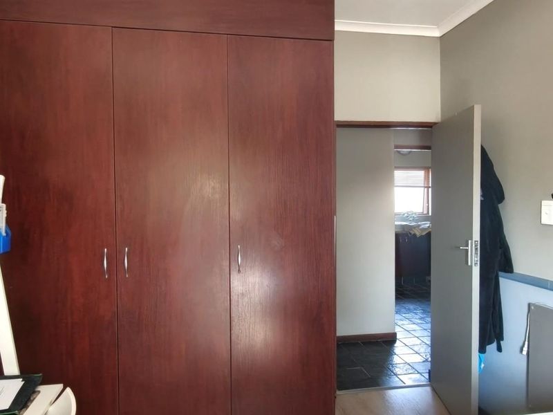 A bedroom featuring a large built-in wooden wardrobe and access to an adjoining room with tiled flooring.