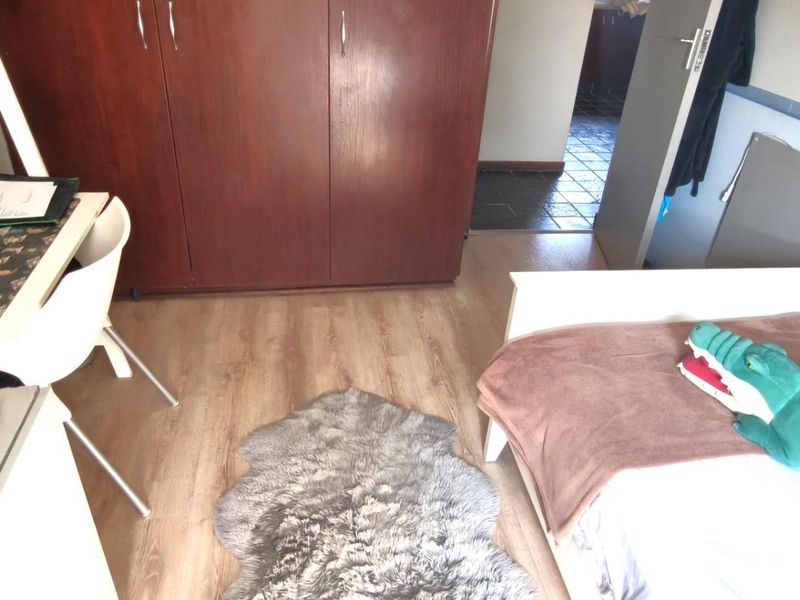 A functional bedroom featuring laminate flooring and a built-in wooden wardrobe, providing practical storage space.