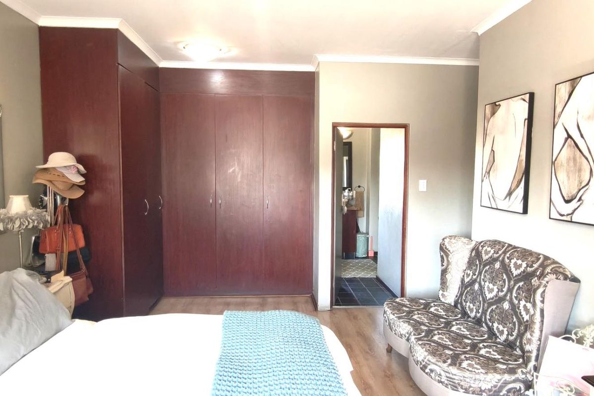 A bedroom featuring built-in dark wood cupboards, laminate flooring, and direct access to an en-suite bathroom.