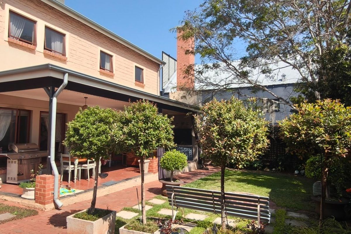 Rear exterior view featuring a covered patio with brick paving, a built-in braai, and a well-maintained garden area.