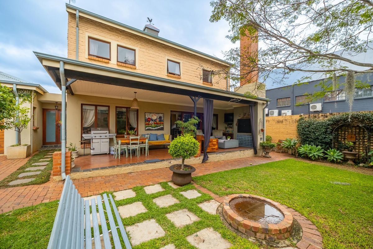 Spacious rear exterior featuring a covered patio, brick paving, a built-in fire pit, and a well-maintained garden area.