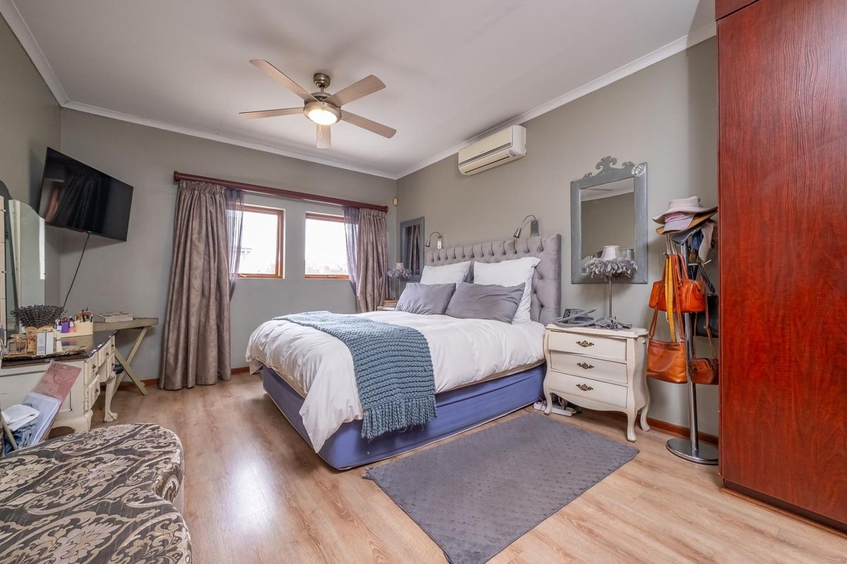 A well-maintained bedroom featuring laminate flooring, a ceiling fan, and a wall-mounted split-system air conditioner for climate control.