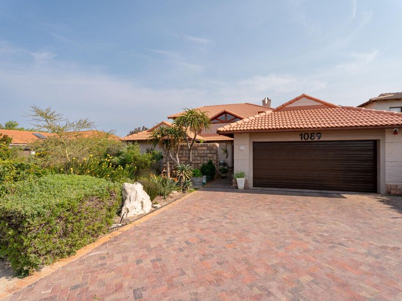 Front elevation of a well-maintained residence featuring a brick-paved driveway, double garage, and established landscaped garden.