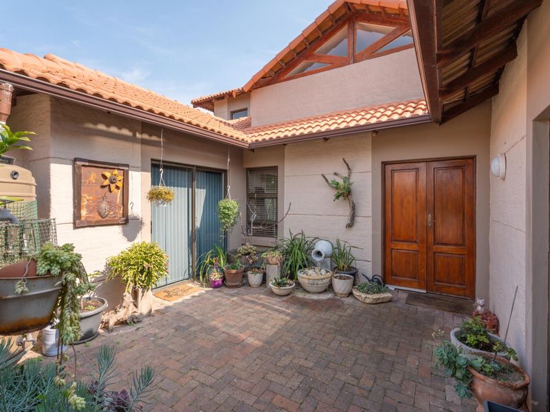 A private brick-paved courtyard featuring terracotta roof tiles, exposed timber trusses, and double wooden entrance doors, providing a charming outdoor transition space.