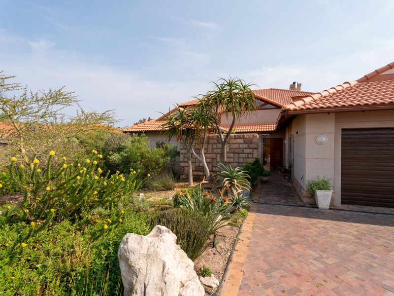 Front elevation of a house featuring a brick paved driveway, stone accent wall, and terracotta tiled roof, surrounded by established garden landscaping.