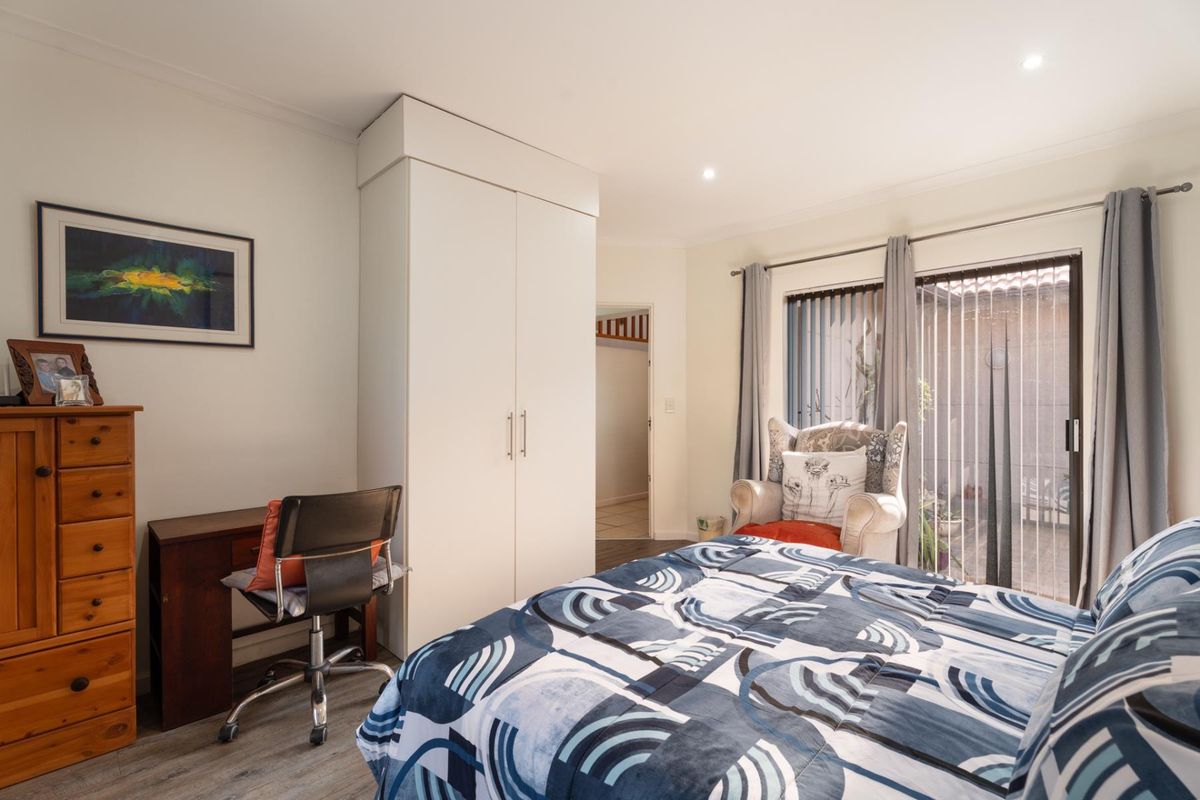 A well-lit bedroom featuring a built-in wardrobe, laminate flooring, and a sliding glass door providing access to the exterior.