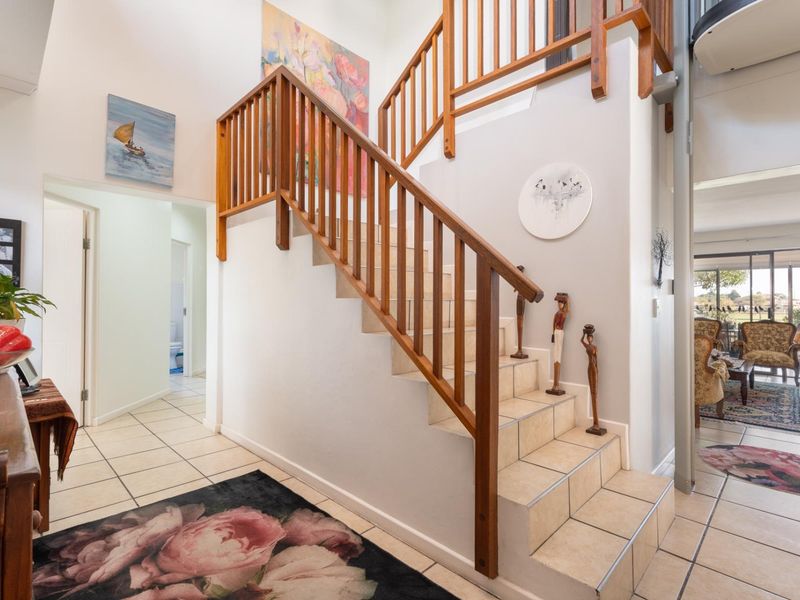 Entrance foyer featuring a central timber staircase with balustrade and tiled flooring, providing access to the living areas and hallway.