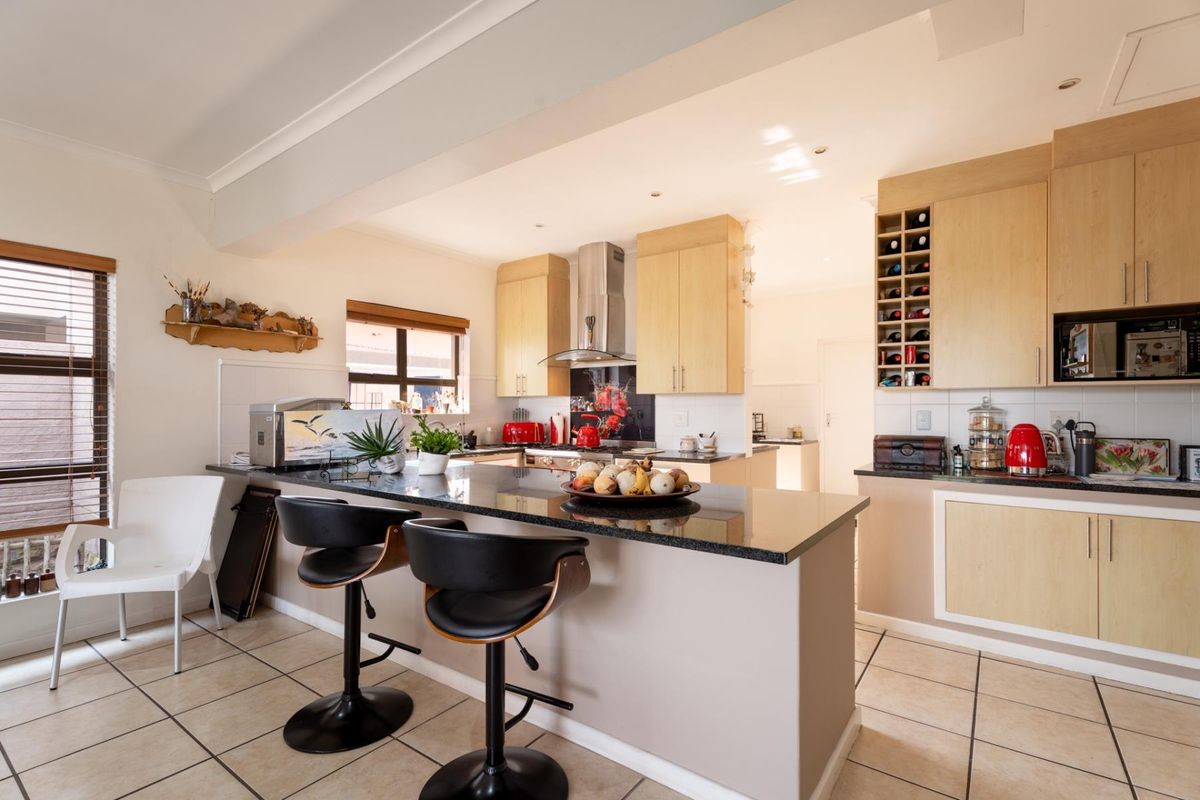 A functional kitchen featuring light wood cabinetry, granite countertops, a breakfast bar, and integrated wine storage, complemented by tiled flooring.