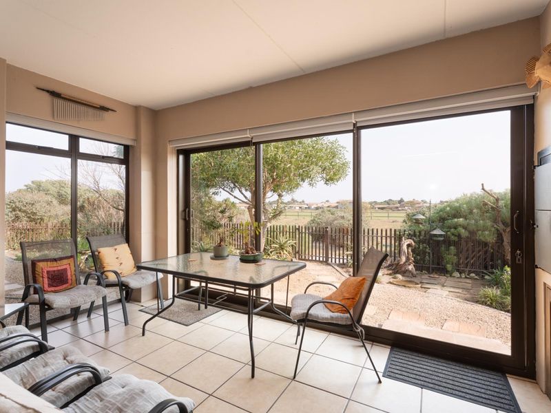 A bright, enclosed patio featuring large sliding glass doors, tiled flooring, and a built-in fireplace, offering views of the rear garden.
