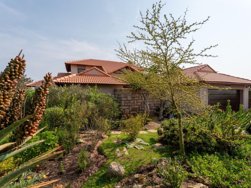 Front view of a residential property featuring a terracotta tiled roof, stone wall accents, and a well-maintained landscaped garden.