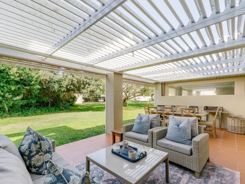 A spacious covered patio featuring a modern louvred roof system and tiled flooring, overlooking a private garden area.