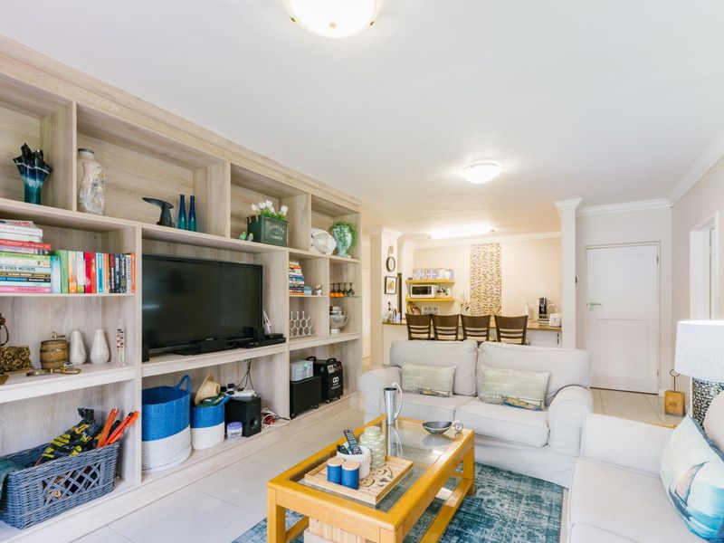 An open-plan living area featuring a large built-in shelving unit, tiled flooring, and a breakfast bar connecting to the kitchen space.