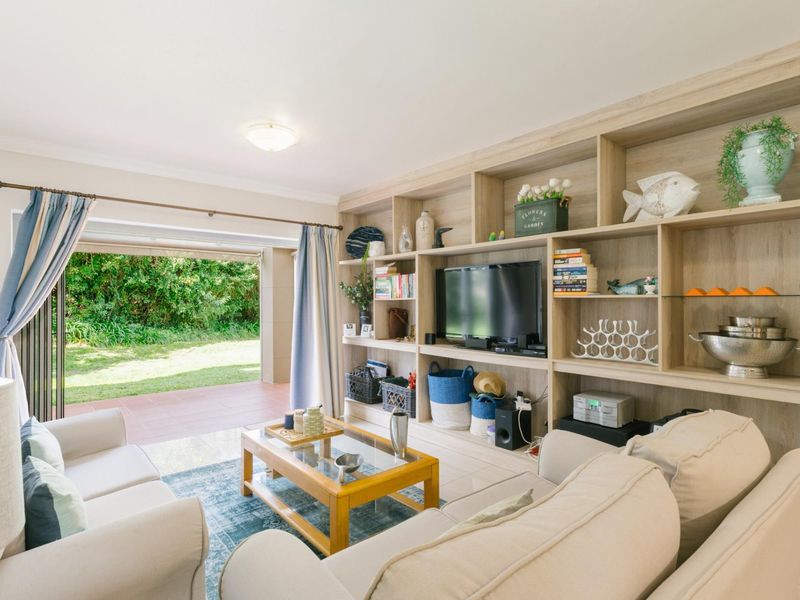 Bright living room featuring a large built-in wooden shelving unit and direct access to a covered patio and garden area through sliding glass doors.