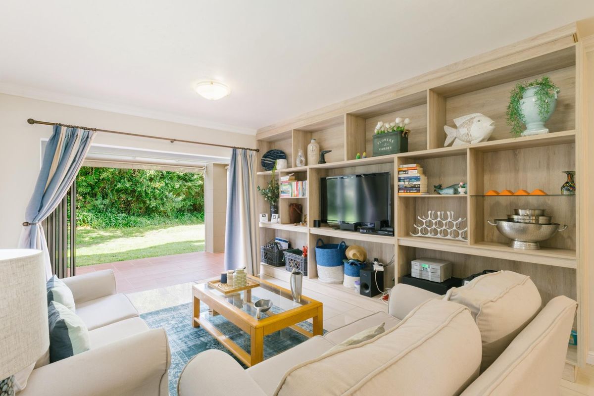 Bright living room featuring a large built-in wooden shelving unit and direct access to a covered patio and garden area through sliding glass doors.