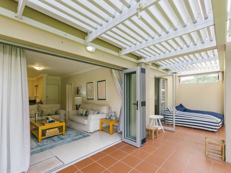 Covered patio area featuring tiled flooring and a white pergola, seamlessly connecting to the interior living space through large bi-fold doors.