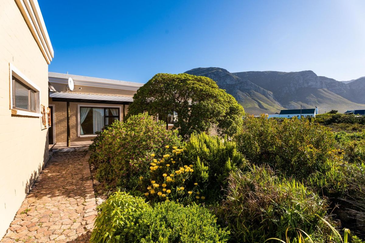 A well-maintained rear exterior view featuring a paved walkway, covered patio area, and established garden with scenic mountain views.