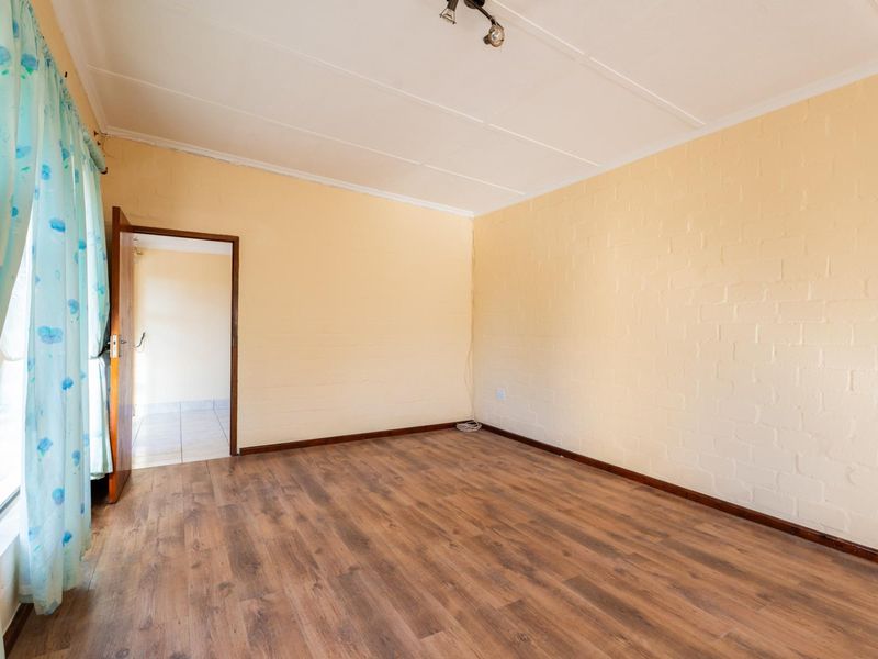 A bright, empty bedroom featuring laminate flooring, painted exposed brick walls, and a simple ceiling light fixture.
