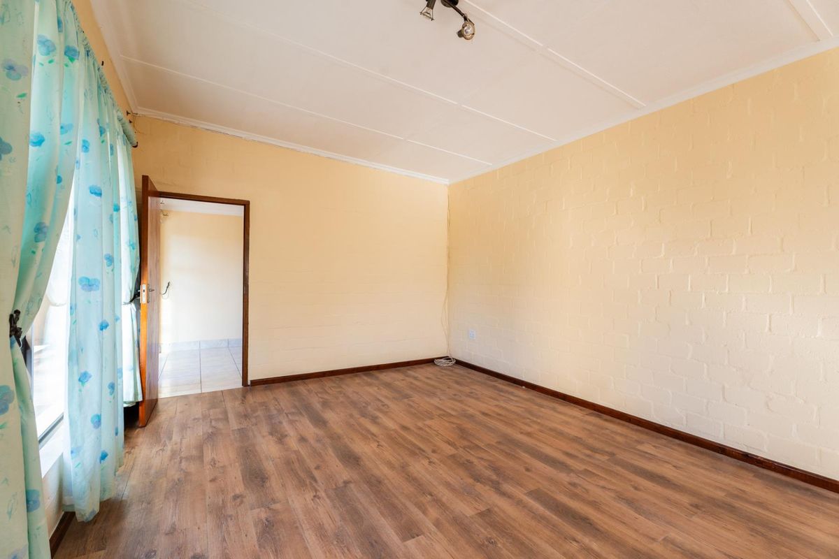 A bright, empty bedroom featuring laminate flooring, painted exposed brick walls, and a simple ceiling light fixture.