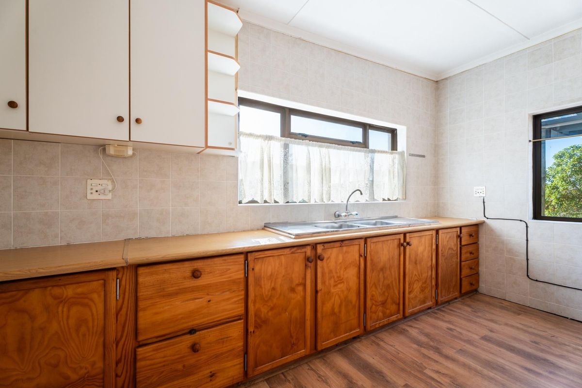 A functional kitchen featuring wooden cabinetry, laminate countertops, a stainless steel double sink, and tiled walls, offering a blank canvas for modern renovation.