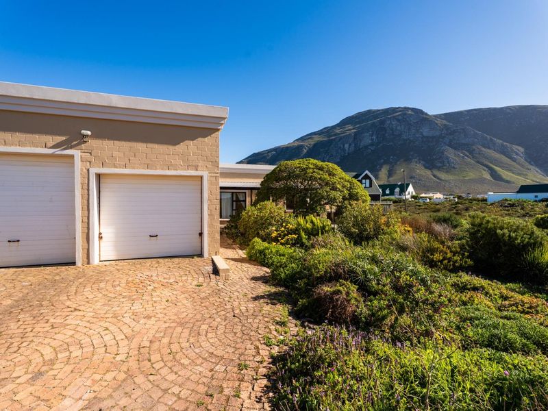Front exterior view of the property featuring a double garage, brick paved driveway, and established garden with scenic mountain views.