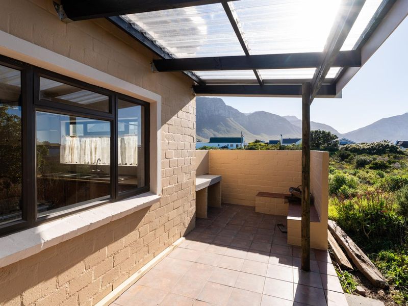 Covered outdoor patio featuring a built-in braai, tiled flooring, and a timber pergola structure with mountain views.