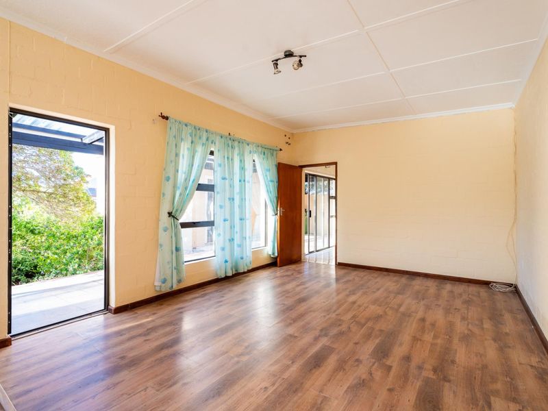 A spacious, empty living room featuring laminate flooring, neutral painted brick walls, and direct access to an outdoor patio area.