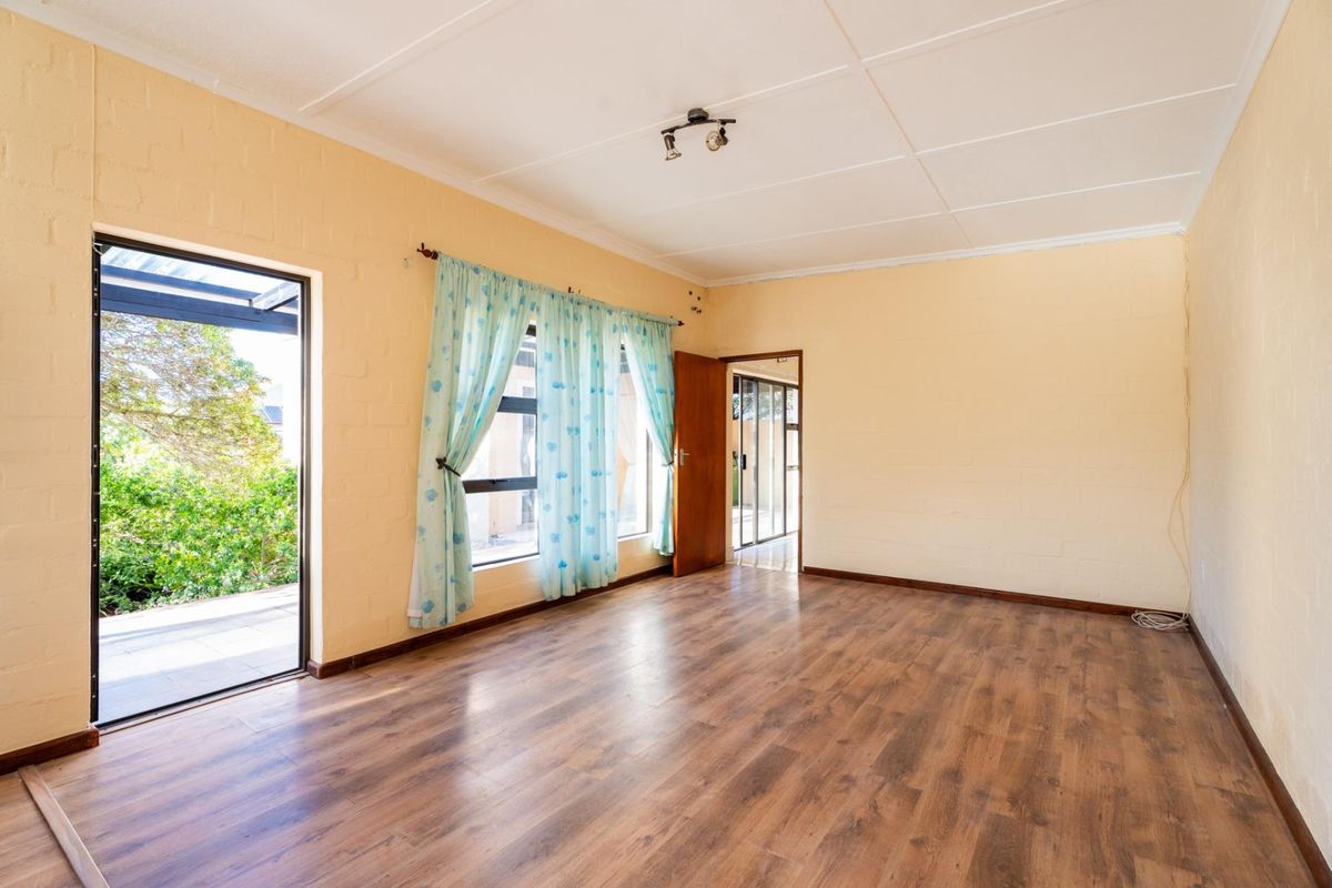A spacious, empty living room featuring laminate flooring, neutral painted brick walls, and direct access to an outdoor patio area.