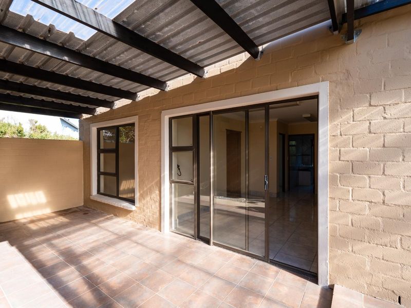 A covered patio area featuring tiled flooring, corrugated roof structure, and sliding glass doors providing access to the interior living space.