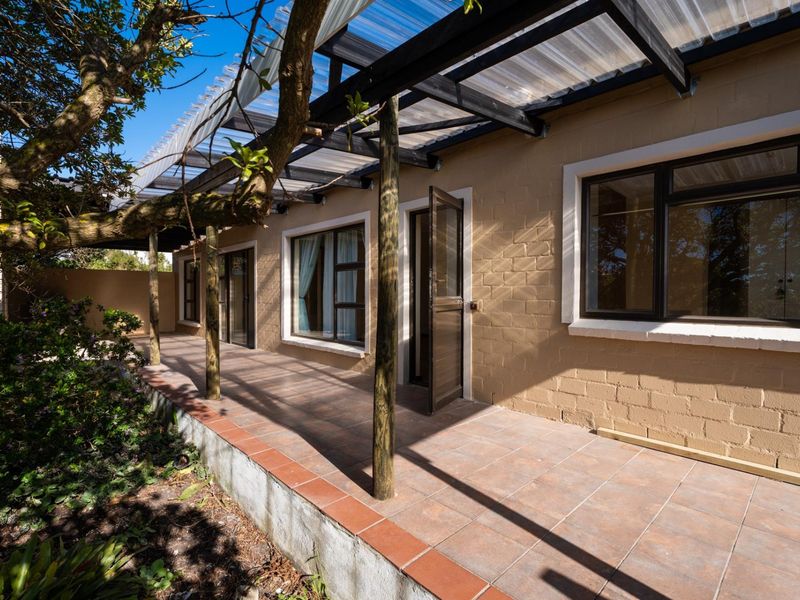 Covered outdoor patio area featuring tiled flooring, timber support posts, and a translucent roof, providing a functional transition space to the garden.