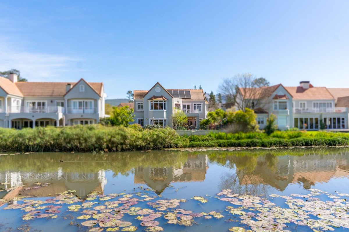 A scenic view of the rear elevation of a residential property featuring a tiled roof, solar panels, and a balcony overlooking a tranquil pond.