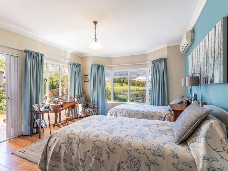 Spacious bedroom featuring hardwood flooring, crown molding, a bay window with garden views, and direct access to an outdoor patio area.