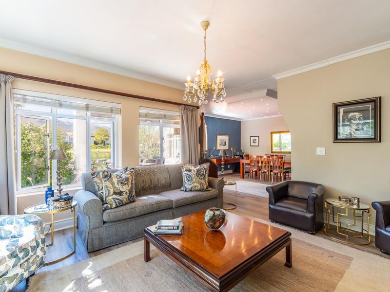 Spacious open-plan living and dining area featuring elegant chandelier lighting, large windows with garden views, and modern laminate flooring throughout.